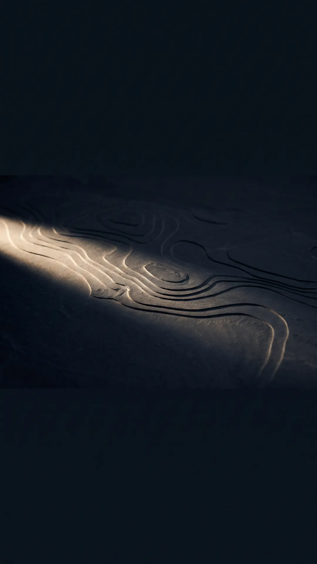 Topographic contour lines carved in relief into dark stone under raking light