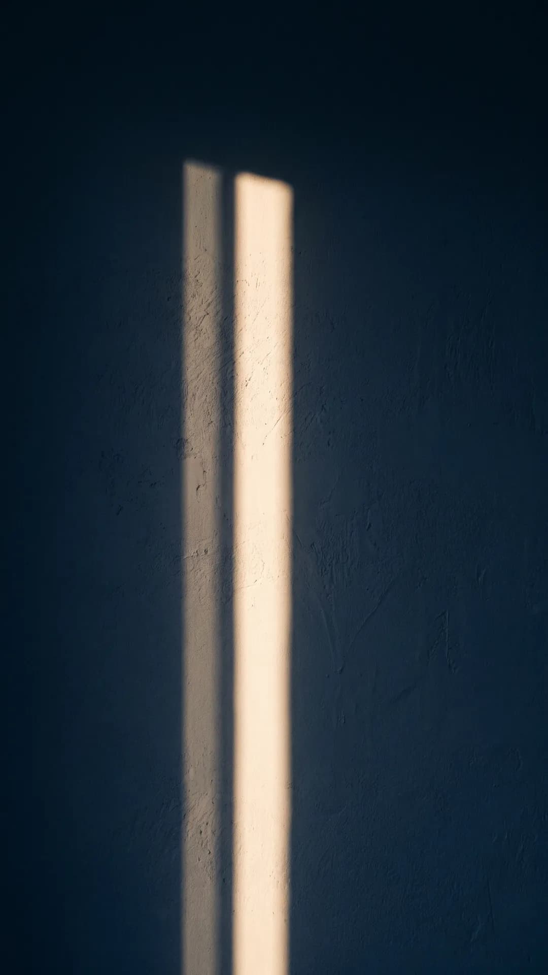 A vertical shaft of warm light across a dark navy wall