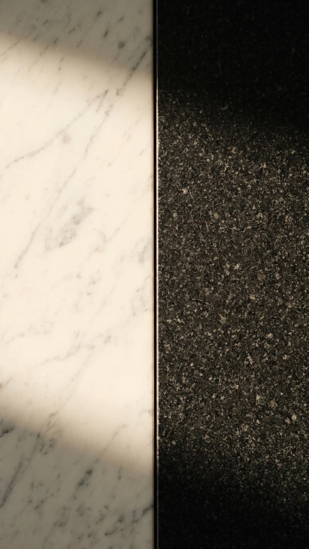 White Carrara marble and dark speckled granite meeting in a vertical seam