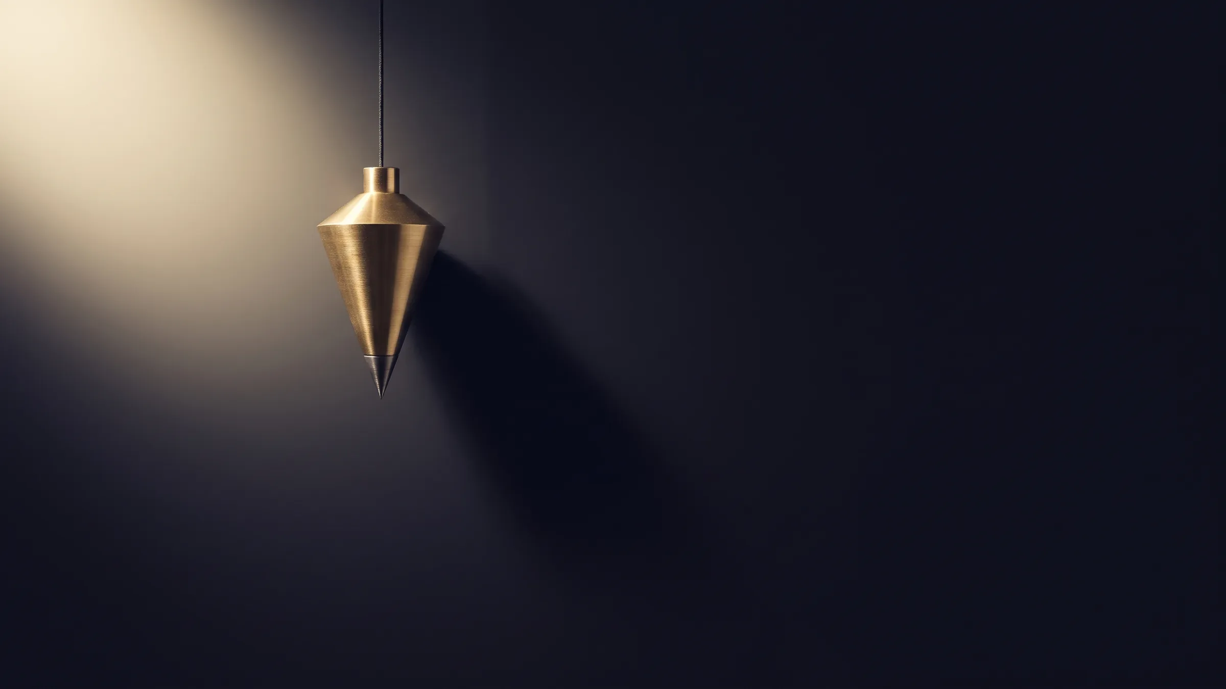 A brass plumb bob hanging on its line in darkness